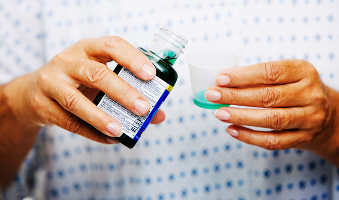 woman-patient-hospital-gown-pouring-medicine-syrup-measuring-cup